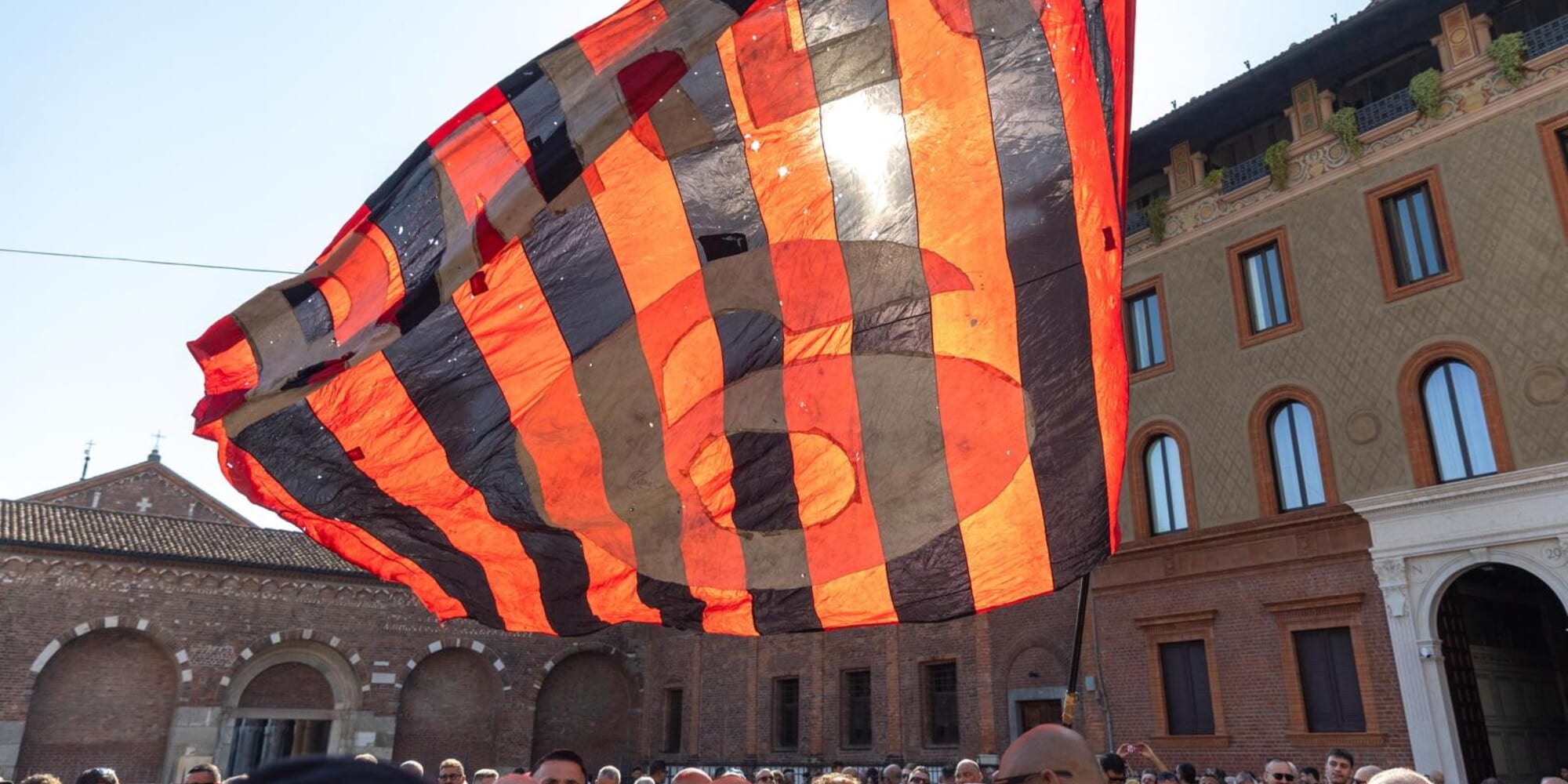 Un corteo di tifosi e personaggi del calcio a Milano, con la bara di Franco Baresi, circondati da folla e bandiere rossonere